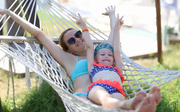 Woman with little girl are joyful swing on deck chair. Spending time with family in nature concept
