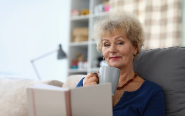 Büyükanne kahve içer ve evde kitap okur. Güzel, yaşlı, emekli kadın. Evdeki kanepeye otur ve dinlen..