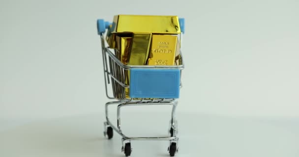 ホワイトバッククローズアップで回転するゴールドバー付きショッピングトロリー 金に対する金融投資 — ストック動画