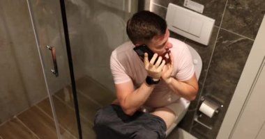 Korkmuş adam telefonda tuvalette sessizce konuşuyor. Koca, akıllı telefonu karısından saklıyor.