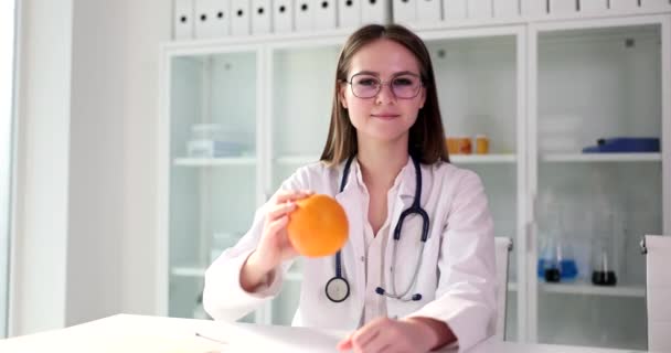 女性医師は柑橘類を手に持っています 化粧品学者栄養士は適切な栄養を推奨しています — ストック動画