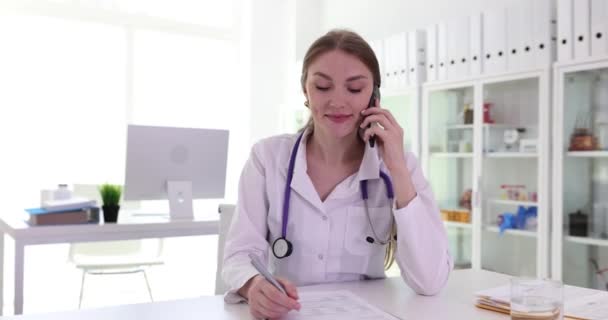 笑顔の女性医師がクリニックの職場で電話で話す リモート患者コンサルティング — ストック動画