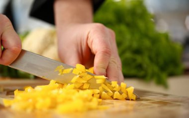 Cook bıçak elinde tutan ve sarı biber salatası veya vitaminler ile taze sebze çorbası için tahta kesme keser. Çiğ gıda ve vejetaryen yemek tarifi kitabı modern toplumun popüler kavram.