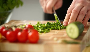 Cook bıçak elinde tutan ve yeşil soğan salata veya vitaminler ile taze sebze çorbası için tahta kesme keser. Çiğ gıda ve vejetaryen yemek tarifi kitabı modern toplumun popüler kavram.