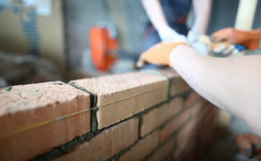 Kolları korumak için özel eldiven giyen yetenekli inşaatçının yakın çekim. Çekiç ile deneyimli yapıcı kırmızı tuğla koymak ve büyük duvar mükemmel yapmak. Bina konsepti