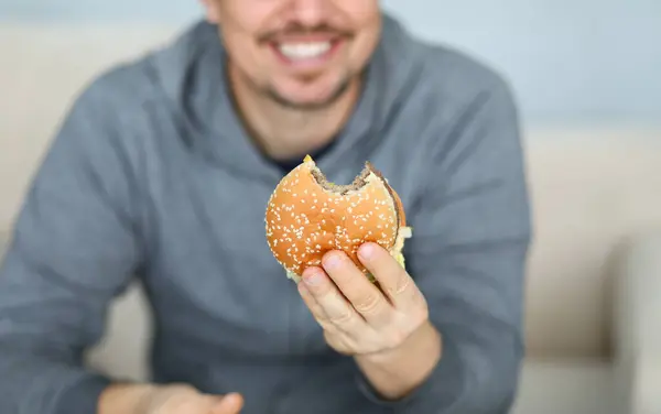 笑顔の男は 手の背景に新鮮なハンバーガーを保持します ファーストフードデリバリーのコンセプト — ストック写真