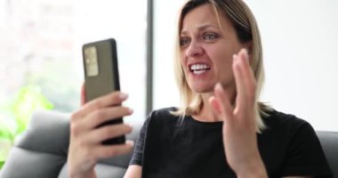 Akıllı telefondan evde küfür eden bir kadın çevrimiçi etkileşimleri izliyor. Akıllı telefon çığlıklarına bakan kadın hayal kırıklığına uğramış ifadesiyle ağır çekimde