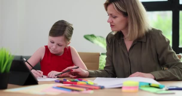 笑顔の母親は小さな娘がアパートの部屋で宿題をするのを助けます スマートな中学生のスローモーションにホームレッスンを実施 — ストック動画