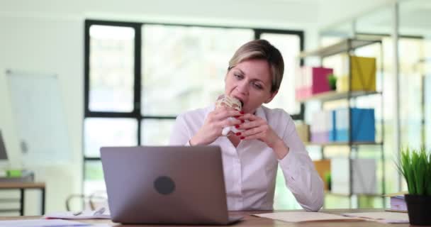 ハンガリーの女性労働者は 会社のオフィスのテーブルでラップトップ画面を見ているシャワーマを食べます 職場でのランチブレイクとテクノロジーコンセプトのスローモーション — ストック動画