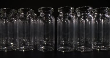 Aşılar için boş cam şişeler karanlık stüdyoda masa yüzeyinde sıra sıra duruyor. Tıbbi amaçlar ve laboratuvar araştırmaları için profesyonel cam eşyalar.