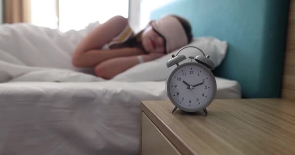 老式闹钟矗立在木制桌子上 在光线充足的前提下 与睡在床上的戴面具女孩相对立 觉醒和梦想概念慢动作的技术 — 图库视频影像