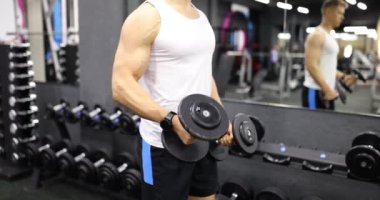 Spor kıyafetli bir sporcu spor salonunda dambılları kaldırıyor. Kas sporcusu ağır halterlerle ayna karşısında ağır çekimde çalışır.