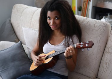 Koyu tenli kız kanepede oturmuş gitar çalıyor. Ellerinde gitarla güzel bir kız. Canlı enstrümantal eşliğinde şarkı. Müzik öğretmeni enstrüman çalmak için materyali gözden geçiriyor