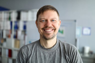 Tişörtlü traşsız adam evde duruyor ve gülümsüyor. Evde otur ve rahatla. Yeni iş haftasından önce biraz soluklan. Kendi kendini izole etmeyi doğru şekilde organize et. Salgın sırasında temel hijyen. Zaman COVID-19