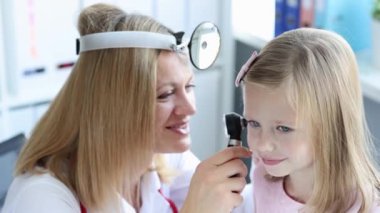 Ön reflektörle, küçük kız kulağını otoskop 4K film yavaş çekim kullanarak inceliyor. Çocuk konseptinde işitme kaybı teşhisi ve tedavisi