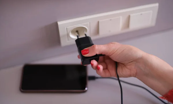 Woman with mobile phone charger in a socket on wall. Charging mobile smartphone concept