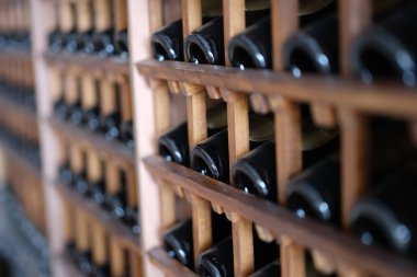 Resting dusty wine bottles stacked on wooden racks in basement. Elite collectible expensive wine in cellar