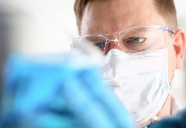 Genç bir cerrah kimyagerin portresi mavi bir sıvıyla kaplara bakıyor ve maske ile virüsler savaşıyor. Hastalıklara karşı aşılar.