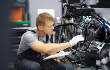 Garajda bir adam motosikleti kontrol ediyor, yakın plan. Parçaları, motoru ve süspansiyonu test edin. Benzin istasyonu uzmanı.