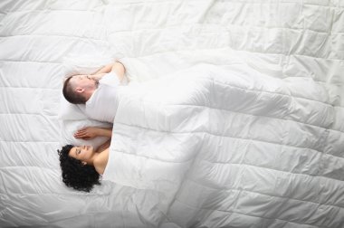 Genç çift büyük, rahat bir yatakta huzur içinde uyuyor. İş gününden sonra huzurlu bir uyku.