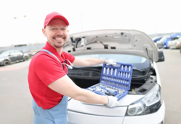 Portrait of young smiling car repairman with set of tools on hood of car. Fast car repair service concept