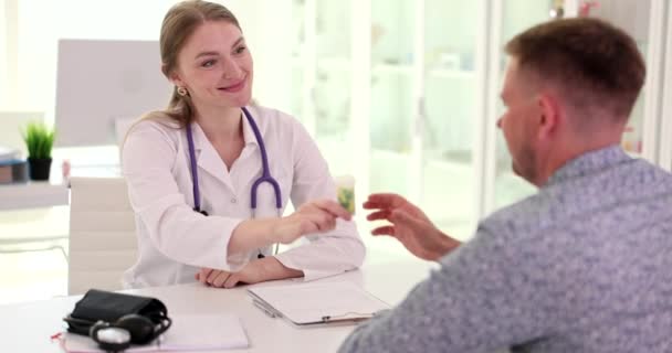 女性医師は クリニックで男性患者に丸薬のボトルを与えます 医療と保険について — ストック動画