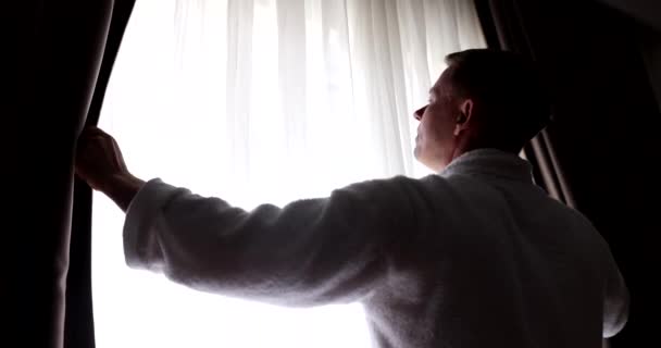 男は窓に立って 手でカーテンを閉める ゆっくり手を動かして部屋のカーテンを閉めると暗くなる — ストック動画