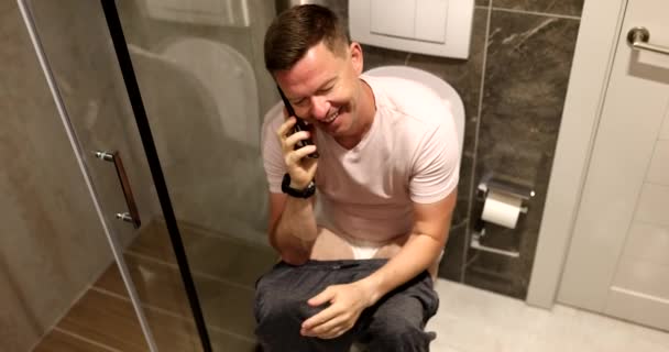 Молодой Человек Разговаривает Телефону Сидя Унитазе Удаленная Связь Туалете — стоковое видео