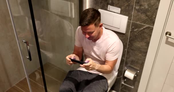 男はスマートフォンを握っているトイレに座っている ガジェット中毒 — ストック動画