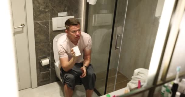 退屈な男はトイレのボウルに座って トイレットペーパーをトイレットペーパーでトイレットペーパーでトイレットバスルームの前に置いた 自然プロセスの遅い動きの概念 — ストック動画