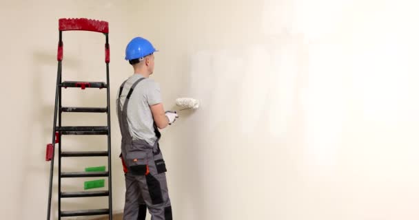 新しいアパートの壁を描くハンディマン 長い棒のローラーを使用してペンキが付いている部屋を飾る建築者の男 インテリアリフォームスローモーション — ストック動画