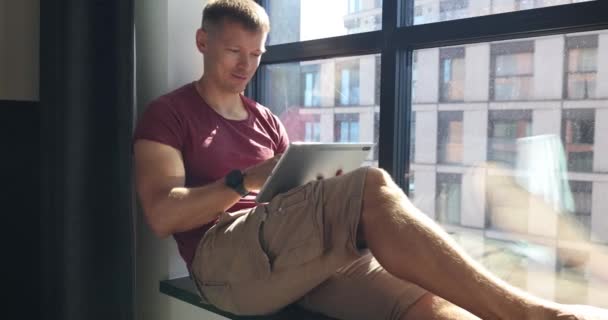 Braunhaariger Mann Der Auf Fensterbank Sitzt Arbeitet Ferngesteuert Mit Laptop — Stockvideo