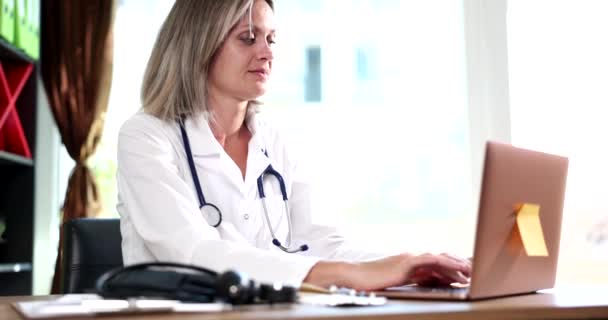 Poważna Lekarka Stetoskopem Pracuje Laptopie Siedzi Przy Stole Szpitalu Terapeuta — Wideo stockowe