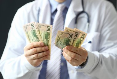 Erkek doktor ellerinin tuttuğu yeşil banknotlara odaklan. Beyaz tıbbi üniforma ve steteskop giyen zeki bir doktor. Sağlık ve Klinik Konsepti