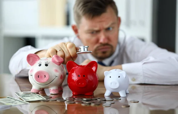 Lustiger Geschäftsmann Hört Drei Sparschweine Für Bargeld Aus Nächster Nähe — Stockfoto