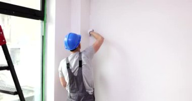 Usta köşedeki duvarı fırçayla beyaza boyar. Duvar onarımı ve boyaması