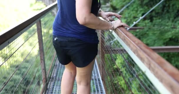 女性の手は 森林の背景に対する橋の柵に触れます パークリザーブの吊り橋 — ストック動画