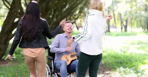 障害者が公園でギターを弾き 2人の女性が踊る 障害者を支援し支援する — ストック動画