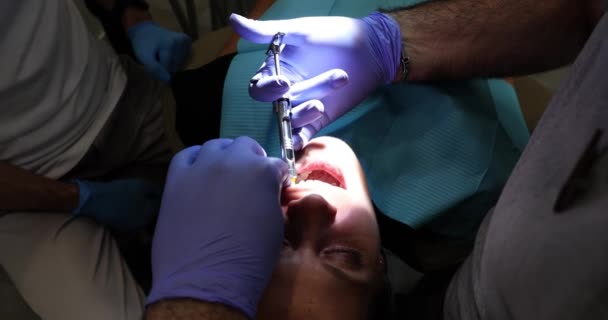 戴医疗手套的牙科医生在牙科诊所给年轻妇女的牙齿注射麻醉 牙科治疗前的镇痛注射及安装防毒面具和假肢 — 图库视频影像