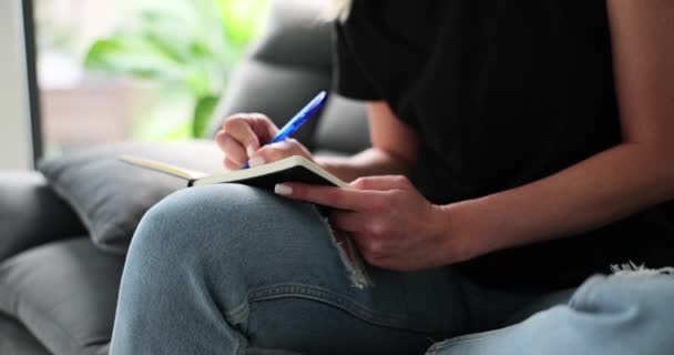 Μια Γυναίκα Κάθεται Στον Καναπέ Και Γράφει Σημειωματάριο Σημείωση Λήψης — Αρχείο Βίντεο