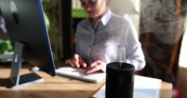 Ofis masasında modern hava nemlendirici aygıtı var. Kadın, aromaterapi buharının tadını çıkarıyor.
