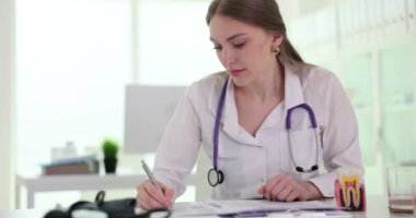 Steteskobu olan profesyonel kadın doktor, klinikteki hasta için reçete yazıyor. Doktor yavaş çekimde muayene odasında.