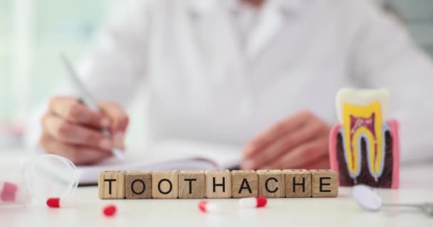 ノートとプラスチック歯モデルを取る医師に対して小さな木製キューブで構成されたWord Toothache クリニックにおける歯痛の歯科治療 — ストック動画