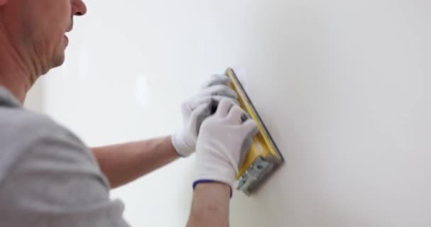 戴手套的承包商刮掉新房间墙壁上不均匀的油灰涂层 建筑工人完成白色表面的抛光 维修的最后阶段 — 图库视频影像