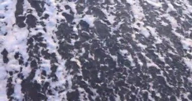 Köpüklü tropikal okyanus dalgaları ıslak siyah kum yüzeyini siler. Kumsalda güneşin batışıyla yanan turist tarafından çizilmiş ünlem işareti.