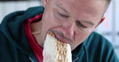 Aç adam bulanık arka planda ışık altında oturarak shawarma yiyor. Yemek molası ve ev konseptinde fast food yemek ağır çekimde