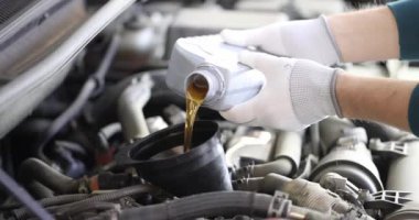 Beyaz pamuk eldivenli erkek işçi işyerindeki şişeden kehribar renkli motor yağı döküyor. Yavaş çekimde otomobil motorunun kayganlaştırıcısı değiştiriliyor
