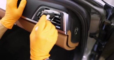 Sarı lastik eldivenli araba bayisi arabanın içindeki kirli klimayı temizlemek için fırça kullanıyor. Araç bakımı ve kirlenmiş parçaların temizlenmesi