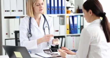 Kadın doktor hastaya klinikteki implantları açıklıyor. Modern ekipmanlarla yavaş çekimde uzmanlaşmak