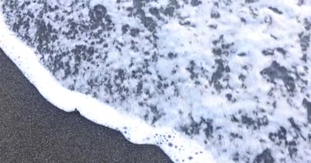 明るい日差しで照らされた茶色のぬれた砂に描かれたテキストエイジ 優しい泡立った波は黒い砂の表面からのビーチのクリーニングの単語を洗います — ストック動画